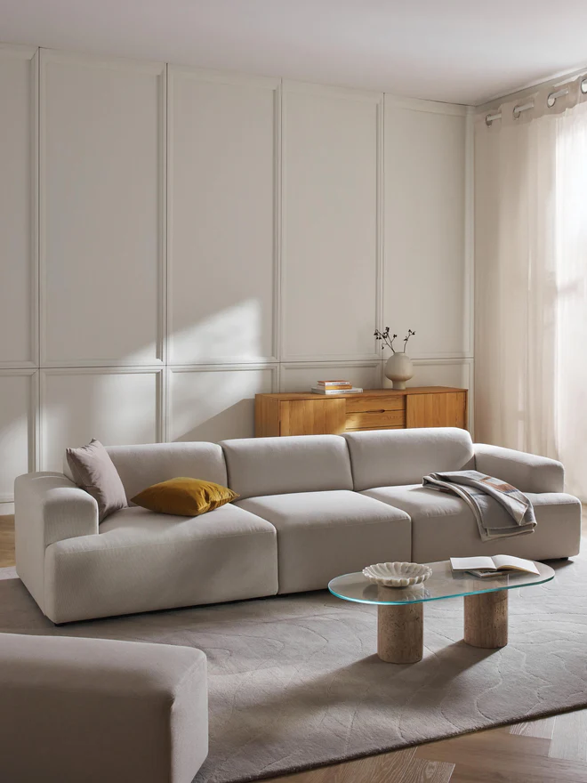 The Melva Sofa (4-Seater) is a spacious and stylish centerpiece for modern interiors. Upholstered in soft, neutral-toned fabric, it features rounded armrests, plush cushions, and a clean low-profile silhouette that emphasizes both comfort and sophistication