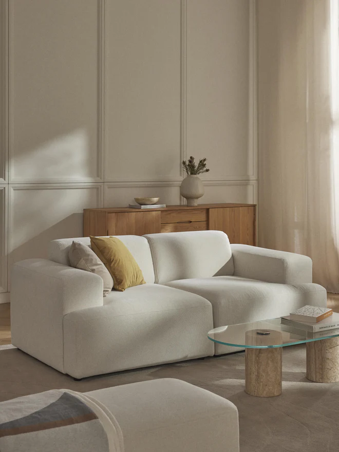 The Melva Sofa (2-Sitzer) offers a refined seating solution for contemporary interiors. Upholstered in soft, textured fabric, it features wide armrests, plush cushions, and a low-profile silhouette that emphasizes both comfort and clean design.