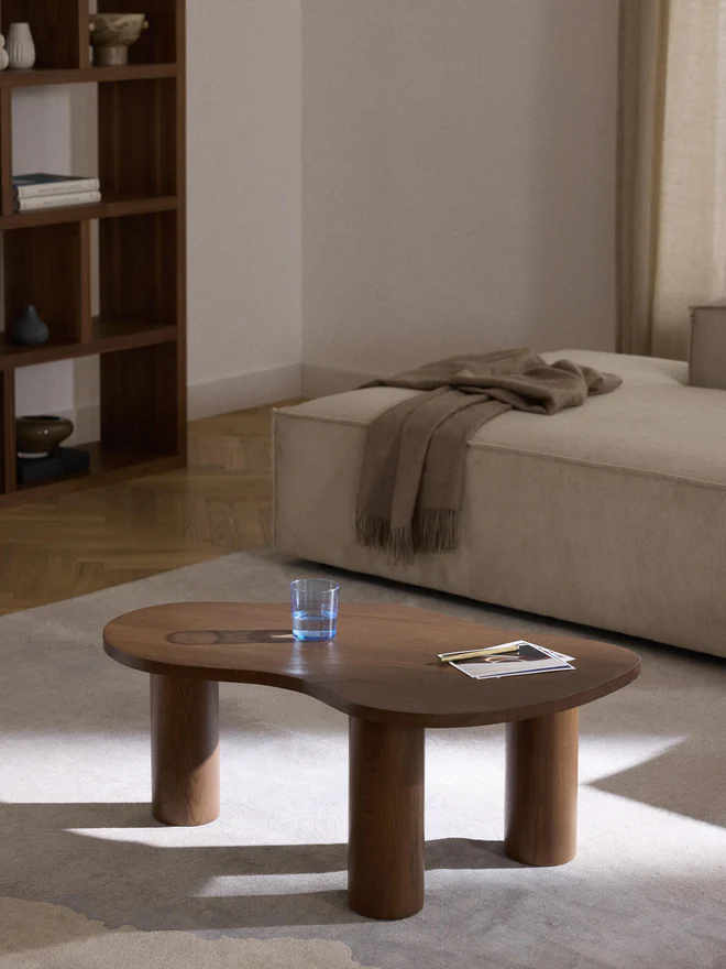 Didi coffee table in solid oak wood with organic shape and round wide legs, available in natural, dark brown, or black finishes