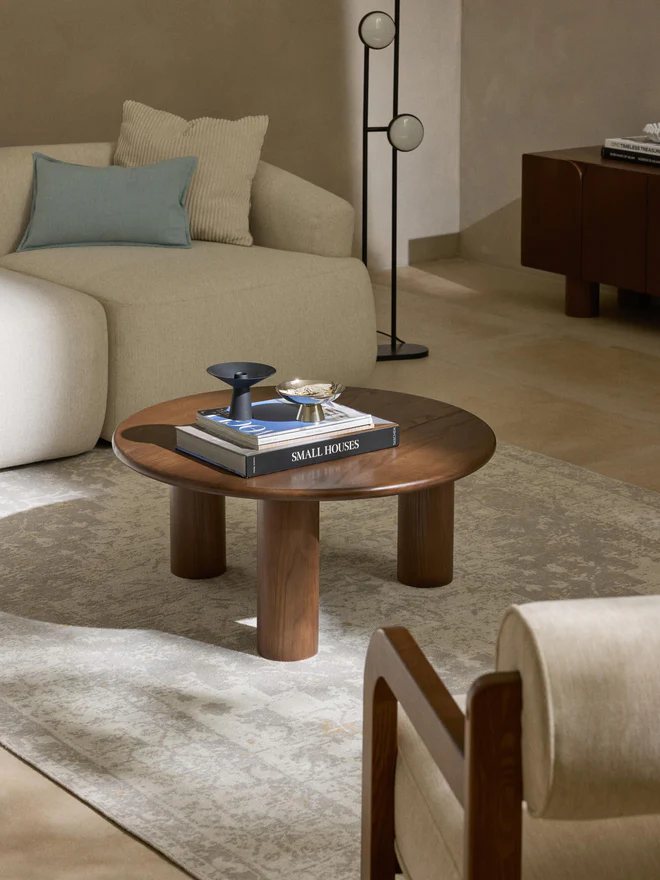 Didi round coffee table in solid oak wood with organic round shape and wide legs, available in natural, dark brown, or black finishes.