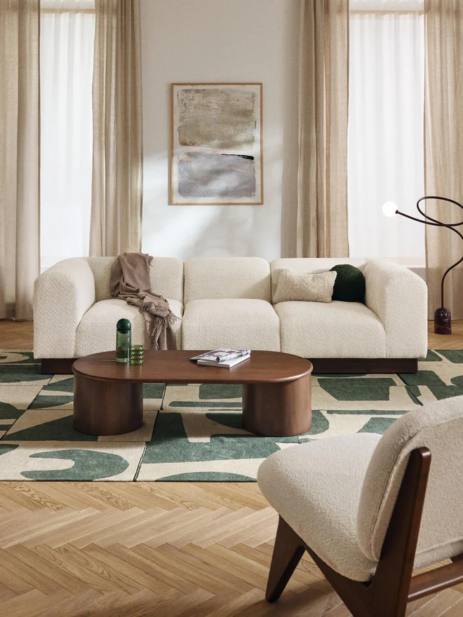 NATALIE modular sofa with rounded design, wooden base, and soft fabric cushions arranged in a contemporary living room.