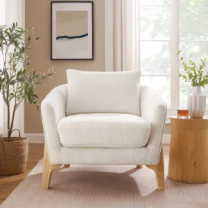 Nordic-style upholstered armchair with textured fabric, pillow back, recessed arms, and natural wood legs in a modern living space