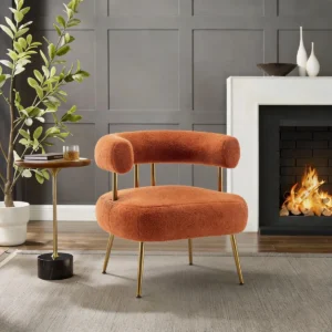 Tufted accent armchair with soft upholstery, rounded arms, and gold-accented metal legs in a modern living space.